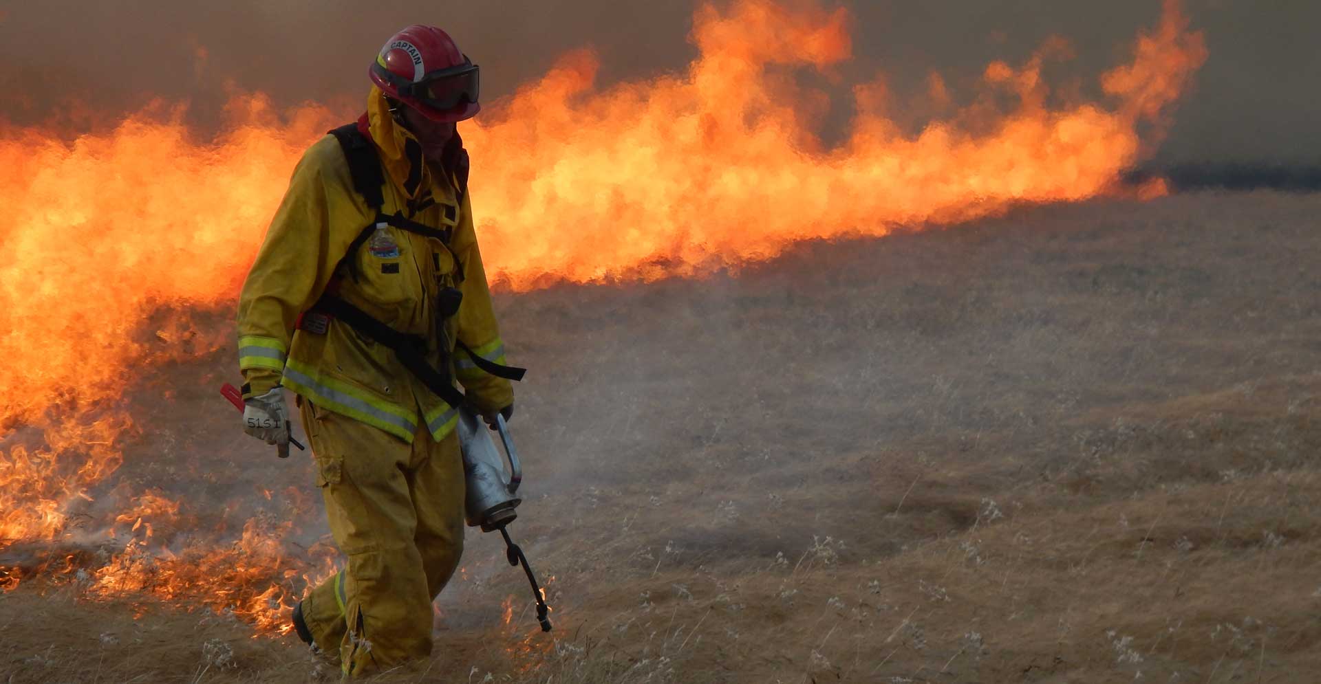 A firefighter lights browned grass on fire in a field for a control burn